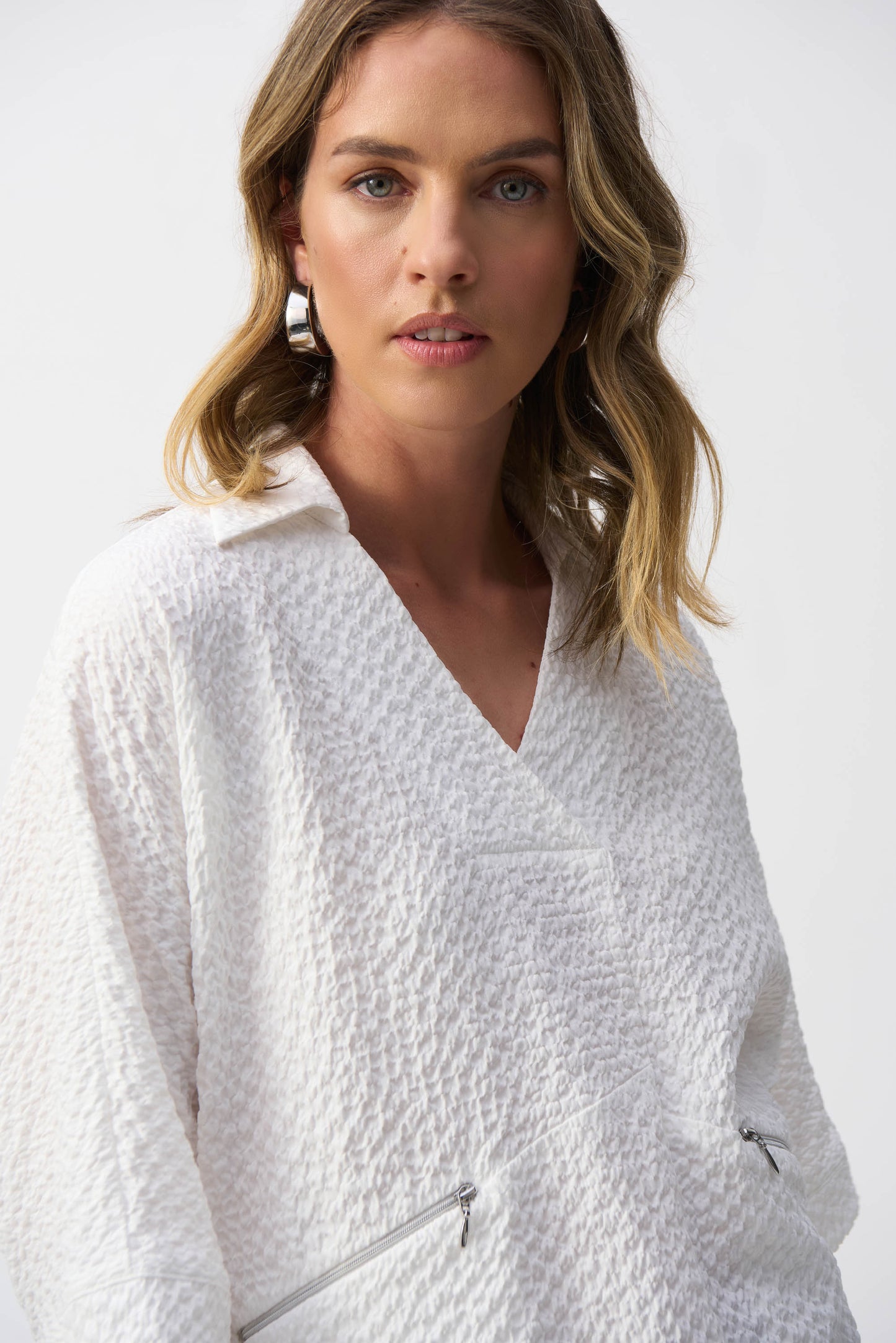 Joseph Ribkoff pullover featuring a chic, minimalistic design with a textured seersucker finish. This hip-length, relaxed-fit piece offers a sophisticated V-neckline, short 3/4 drop sleeves, and front pockets for added functionality. Unlined for a lightweight feel, making it perfect for casual or office wear. Crafted from a soft blend of polyester, viscose rayon, and spandex for comfort and elegance.