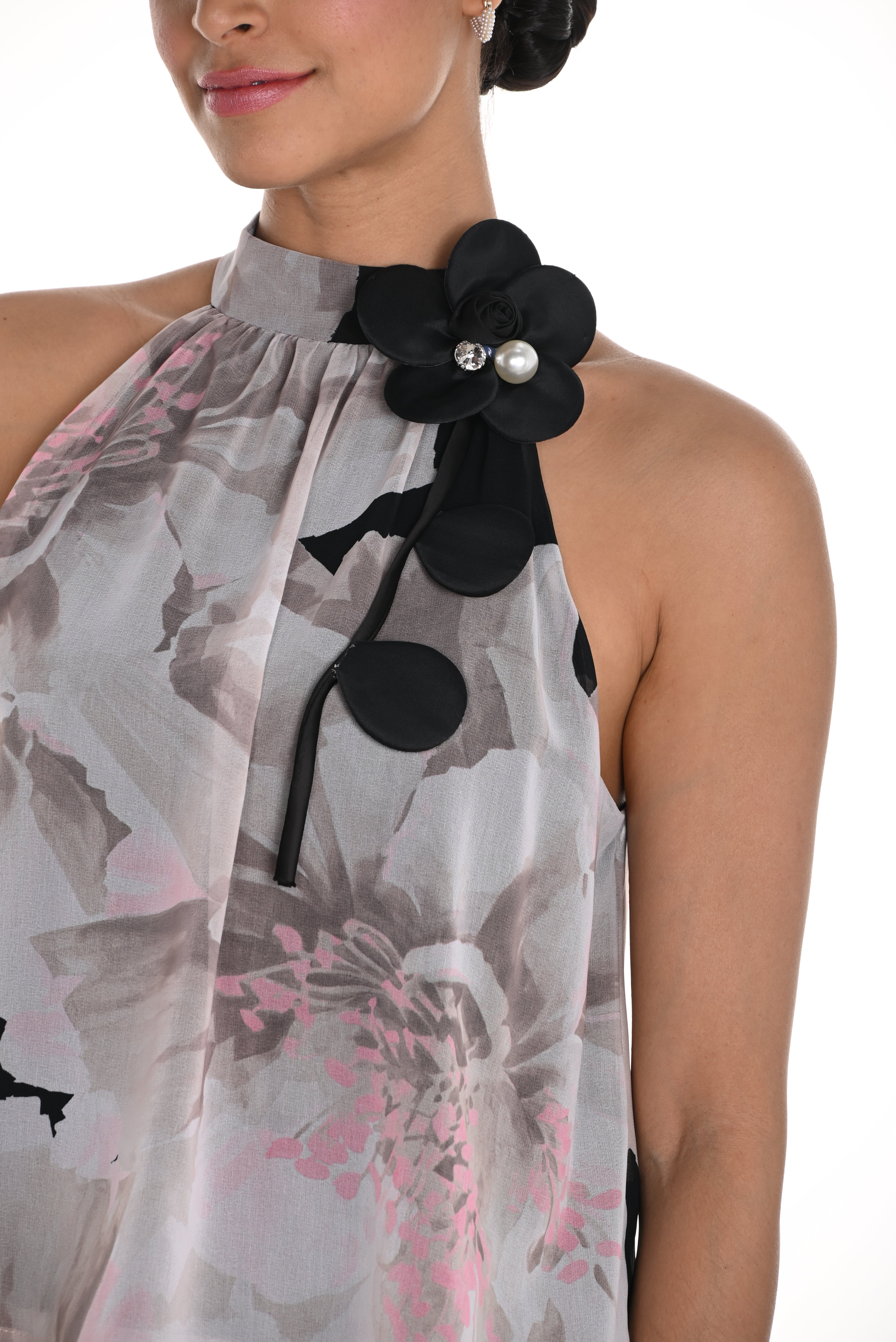 Pearls Boutique-Port Dover Ontario- Frank Lyman Halter Top- Soft pink/grey/black/white floral print, featuring a mock neck, removable floral pin, keyhole back, tiered silhouette, and tunic length. Sleeveless design adds a sophisticated and versatile touch to any outfit.