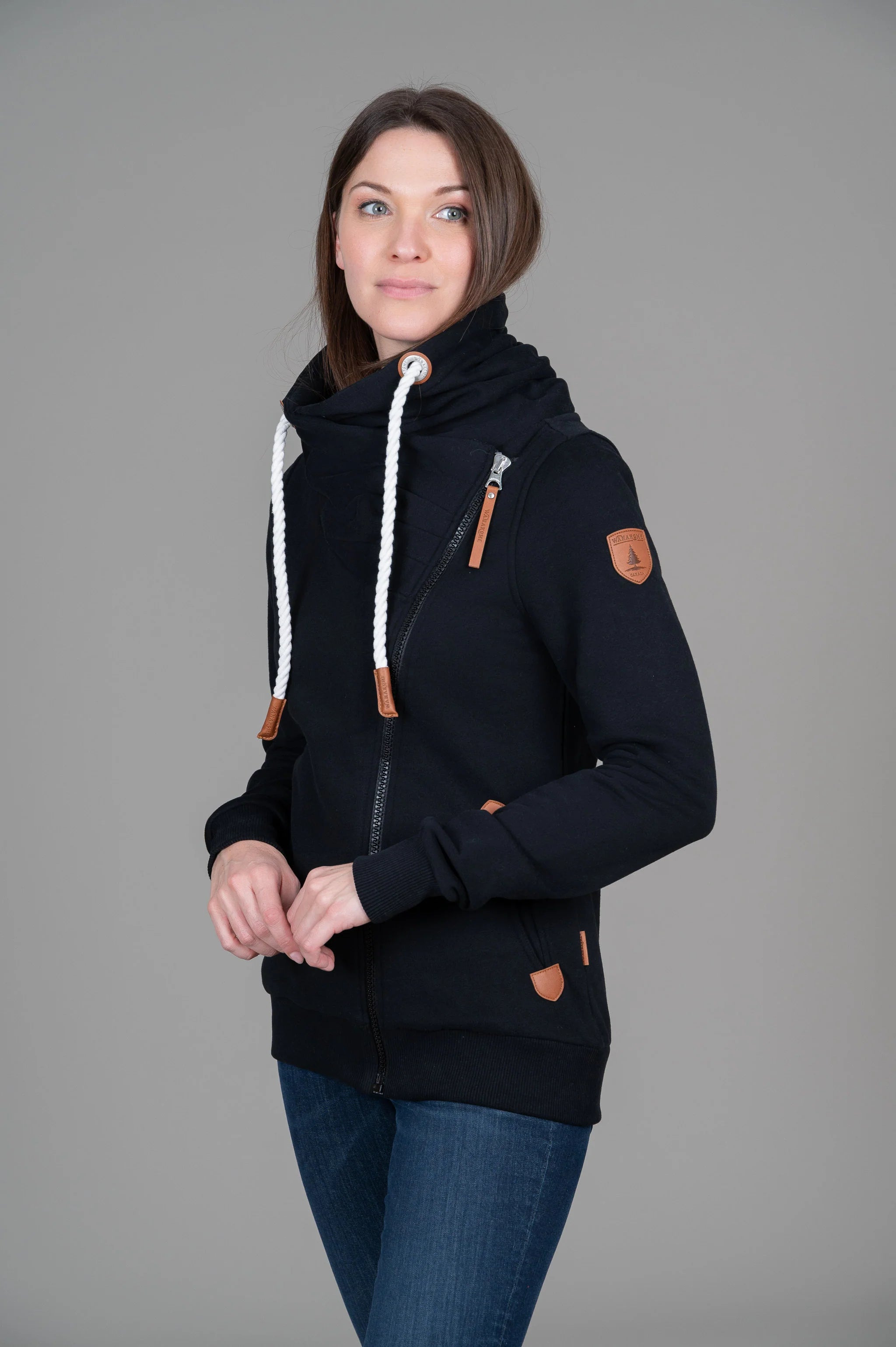 Pearls Boutique-Port Dover Ontario-Wanakome Hestia full-zip sweatshirt-Black. featuring a contoured fit and soft French terry fabric with a brushed interior. Includes an adjustable hood with thick rope drawstrings and vegan leather caps, a full-length asymmetrical zipper, and ribbed cuffs and hem. Finished with vegan leather Wanakome patch logos on the chest and sleeve, plus roomy front pockets for added comfort.
