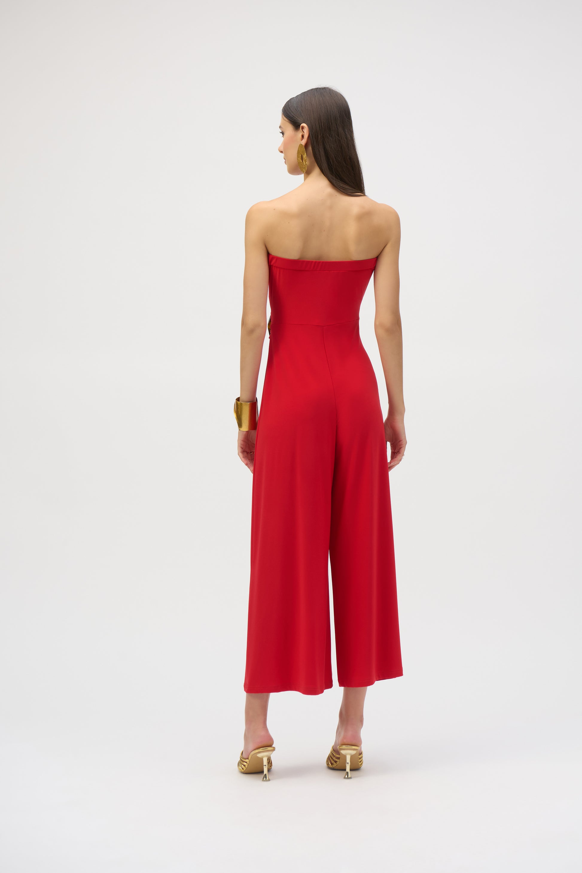 Pearls Boutique- Port DoverOntario-Joseph Ribkoff- Red silky knit strapless culotte jumpsuit-252083 featuring a bandeau-style bodice with hidden elastic for a perfect fit. Designed with a faux wrap detail and a wide-leg silhouette that adds grace to every movement, the side is elegantly draped and adorned with a faux tortoise shell buckle for a dramatic flair. Unlined for a lightweight feel. Made from 95% polyester and 5% spandex, with easy-care instructions: hand wash, hang to dry, and low iron if needed.