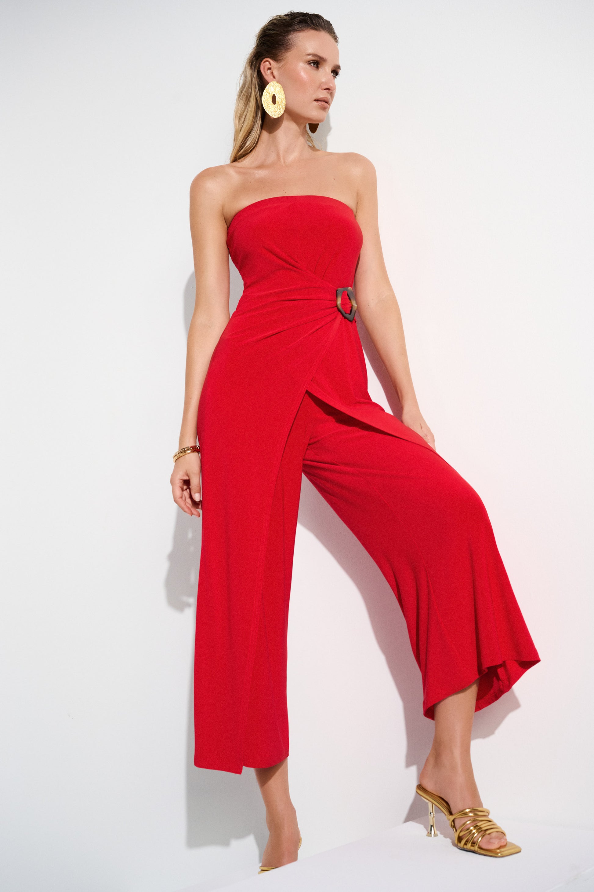 Pearls Boutique- Port DoverOntario-Joseph Ribkoff- Red silky knit strapless culotte jumpsuit-252083 featuring a bandeau-style bodice with hidden elastic for a perfect fit. Designed with a faux wrap detail and a wide-leg silhouette that adds grace to every movement, the side is elegantly draped and adorned with a faux tortoise shell buckle for a dramatic flair. Unlined for a lightweight feel. Made from 95% polyester and 5% spandex, with easy-care instructions: hand wash, hang to dry, and low iron if needed.