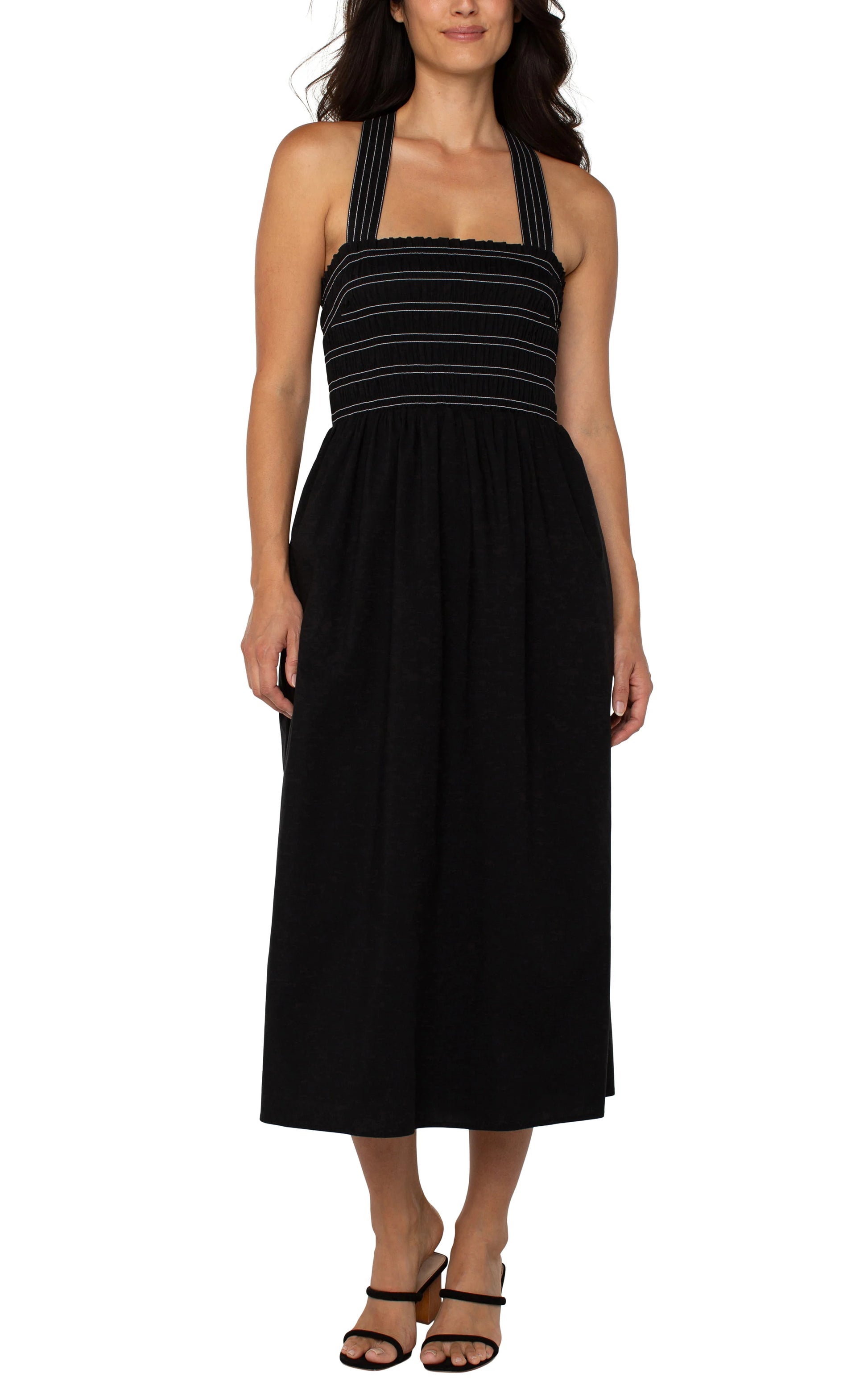 Pearls Boutique|Port Dover Ontario| Liverpool|Sleeveless Smocked Midi Dress|Black with white  stripe accent on straps and bodice.
A sleeveless black midi length dress featuring a smocked bodice with white detailing. The dress has removable shoulder straps, two side pockets, and an A-line silhouette. Made from a blend of 67% cotton, 29% polyester, and 4% spandex, it offers a comfortable, stretchy fit. The dress is 42-1/2" from the high point of the shoulder.