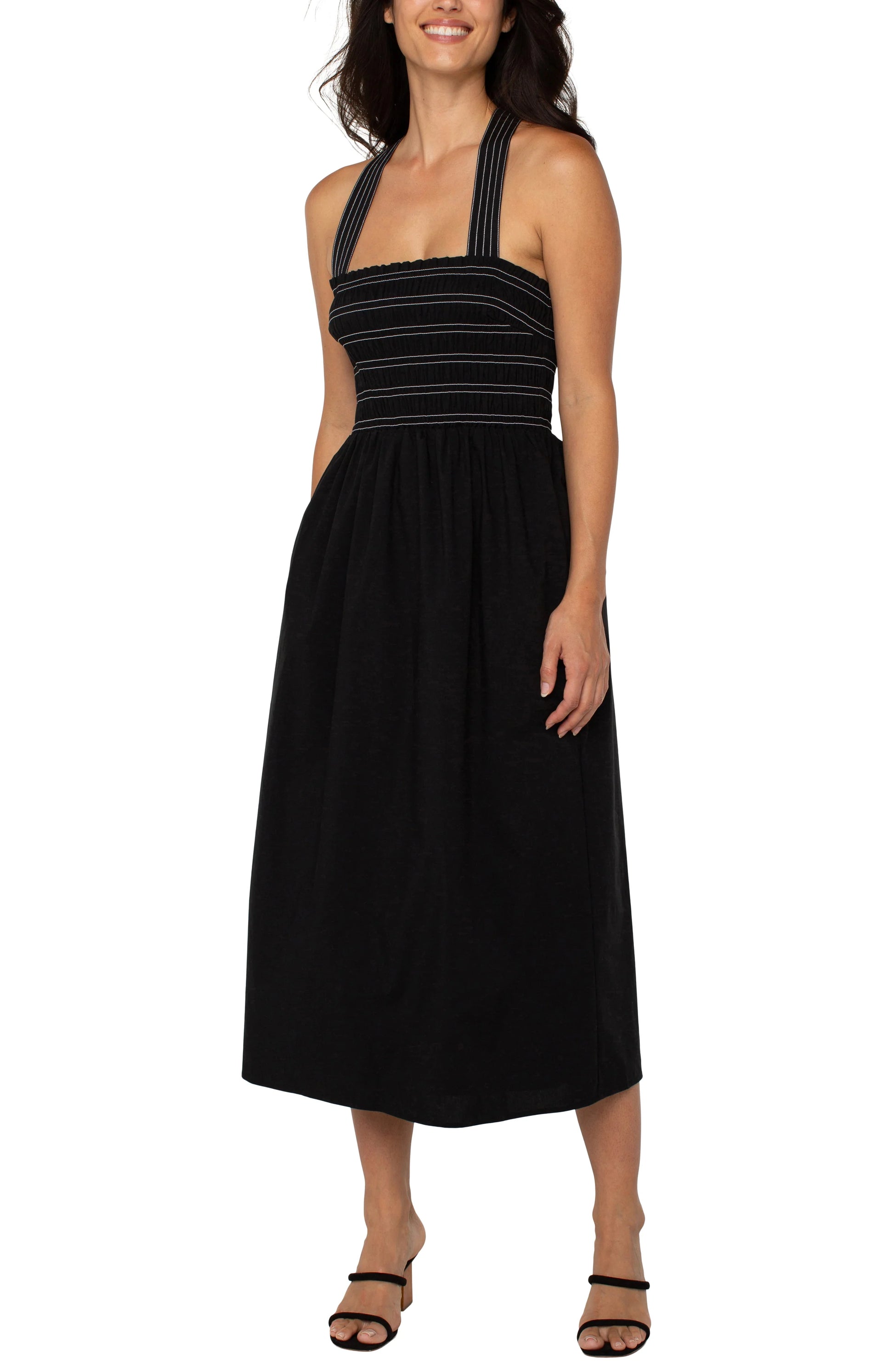 Pearls Boutique|Port Dover Ontario| Liverpool|Sleeveless Smocked Midi Dress|Black with white  stripe accent on straps and bodice.
A sleeveless black midi length dress featuring a smocked bodice with white detailing. The dress has removable shoulder straps, two side pockets, and an A-line silhouette. Made from a blend of 67% cotton, 29% polyester, and 4% spandex, it offers a comfortable, stretchy fit. The dress is 42-1/2" from the high point of the shoulder.