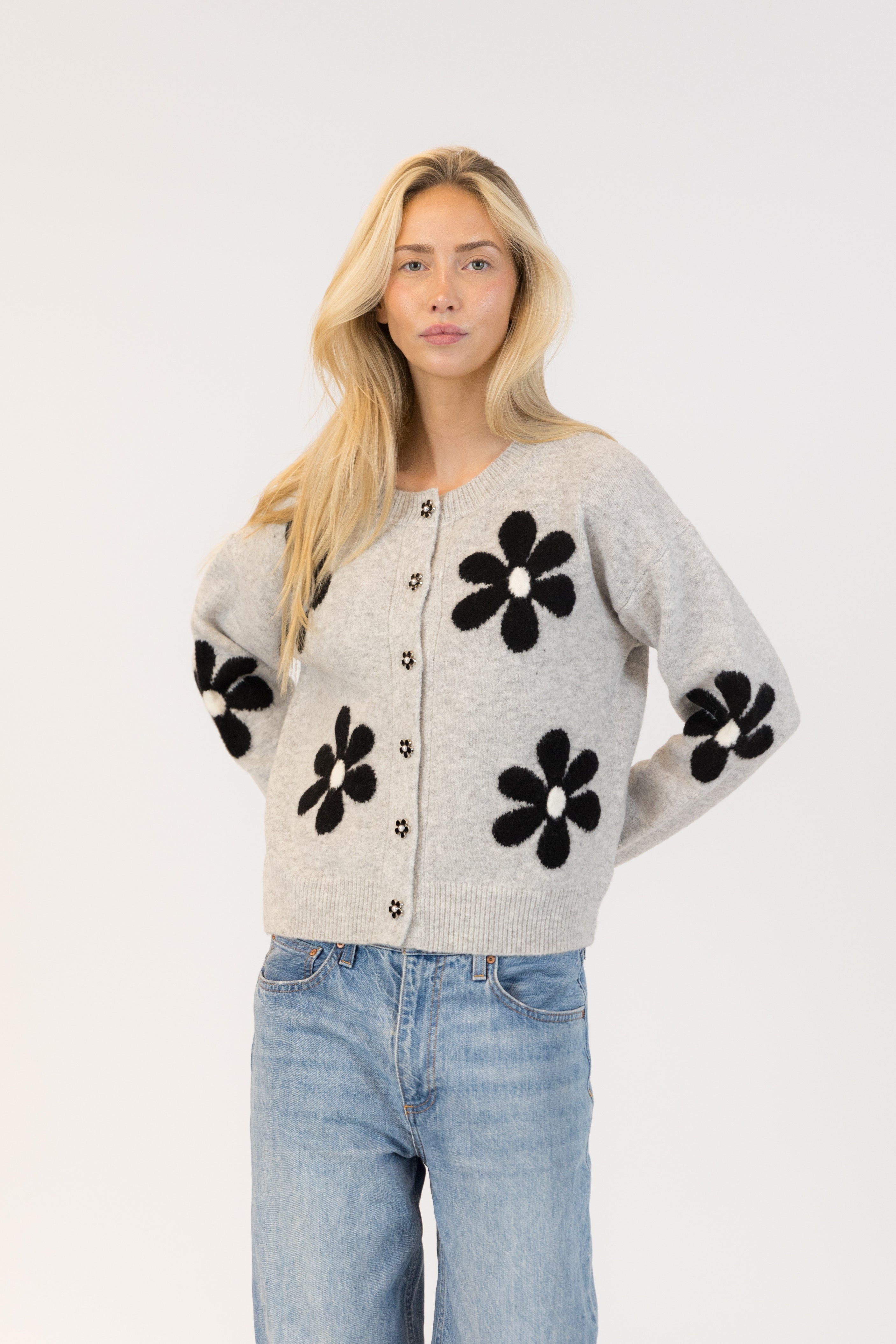 Pearls Boutique| Port Dover Ontario|Lyla + Lux|Lyla + Lux women’s crew neck cardigan named Jorgie, featuring black daisies scattered across a soft  grey melange knit fabric. classic crew neckline, long sleeves, relaxed fit, this cardigan is finished with delicate little black daisy enamel buttons down the front. Crafted from a lightweight, easy-care blend of polyester, acrylic, polyamide, wool, and elastane, 